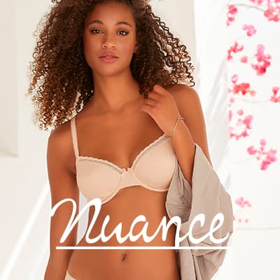 Nuance – Frau in hellem BH und Slip steht im Licht, hält eine offene Bluse locker über der Schulter