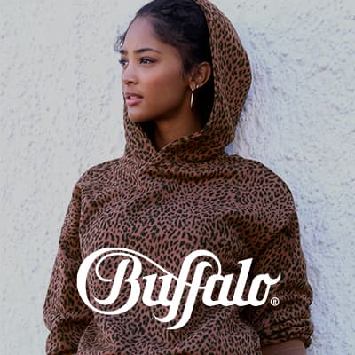 Buffalo Logo – Frau im gepunkteten Kapuzenpullover steht seitlich vor heller Wand