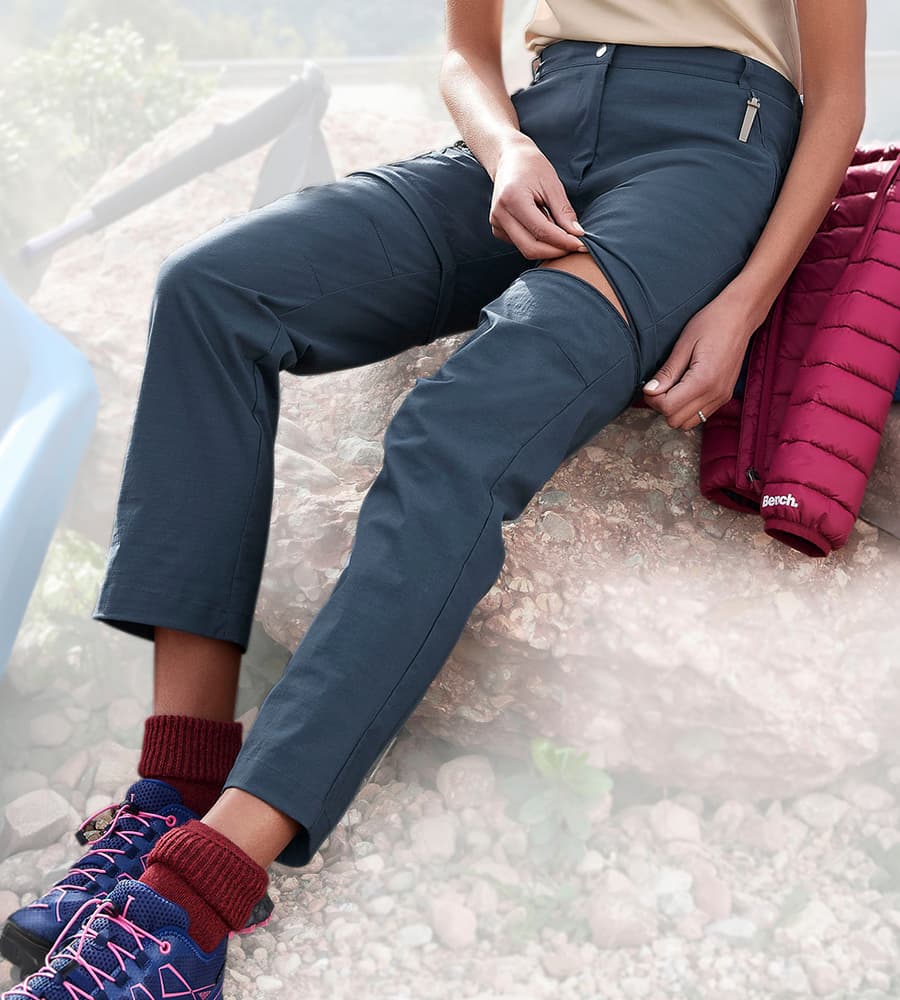 Pantalon de randonnée zippé en bas de jambe, porté par une personne assise avec veste pliée et chaussures de marche