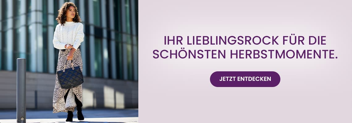 Ihr Lieblingsrock für die schönsten Herbstmomente – Frau im langen Rock mit Tasche geht vor einem modernen Gebäude