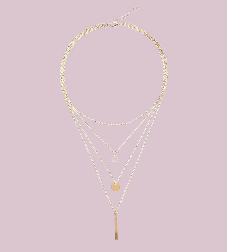 Collier doré à plusieurs rangs avec pendentifs géométriques, sur fond violet clair