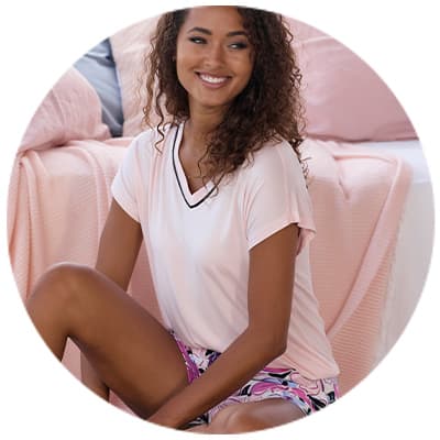 Femme assise en pyjama rose et violet, devant un lit avec couverture rose