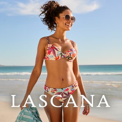 Femme en bikini à motifs colorés, marchant sur une plage avec une serviette à la main – Texte « LASCANA » en bas