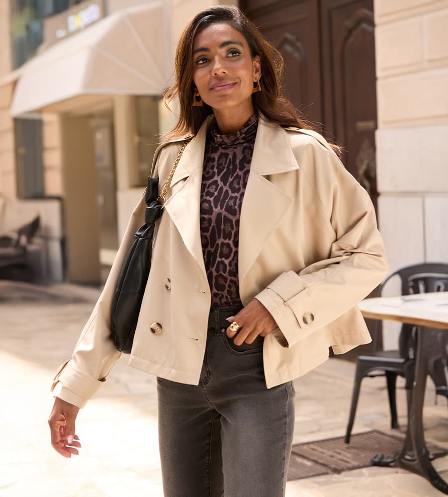 Femme en veste courte beige, top à motif animal, jean gris et sac noir, marchant en ville