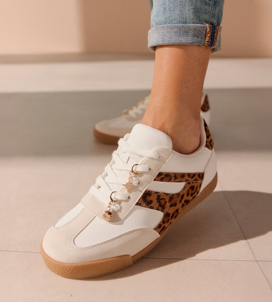 Weiße Sneaker mit seitlichem Leopardenmuster und kleinen Anhängern an den Schnürsenkeln, getragen zu hochgekrempelter Jeans