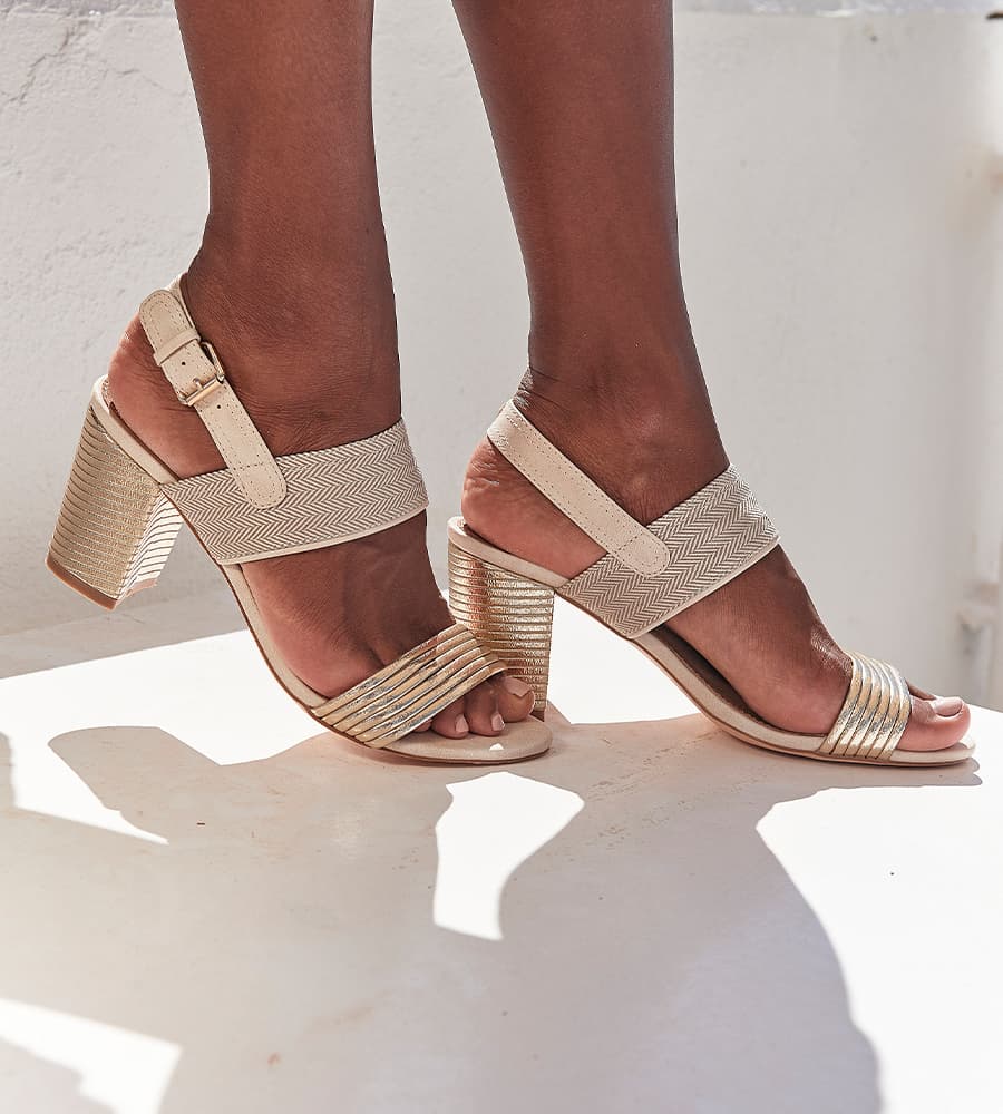 Sandales à talons blocs beiges et dorés, avec bride cheville réglable, portées en extérieur en pleine lumière