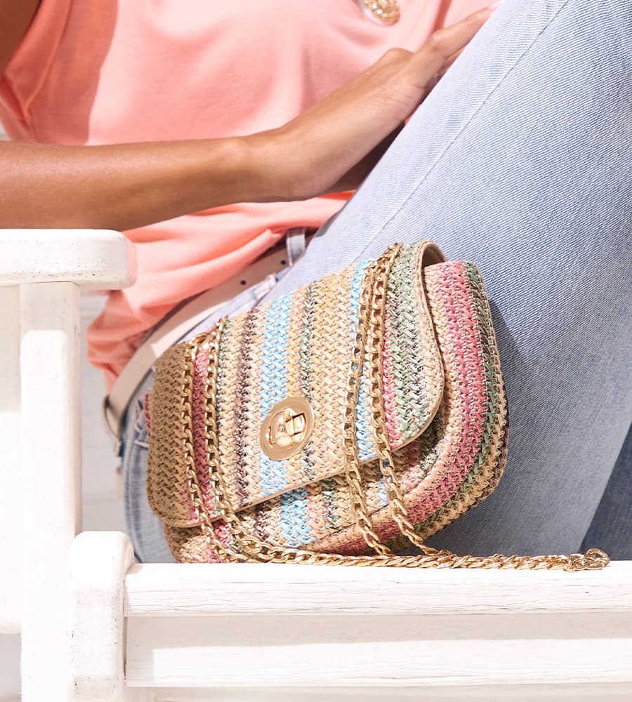 Sac bandoulière à rayures multicolores avec chaîne dorée, porté par une personne en jean clair et top rose