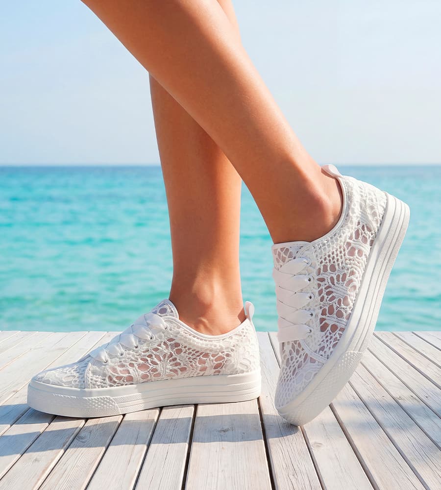 Baskets blanches ajourées portées sur un ponton en bois devant la mer turquoise