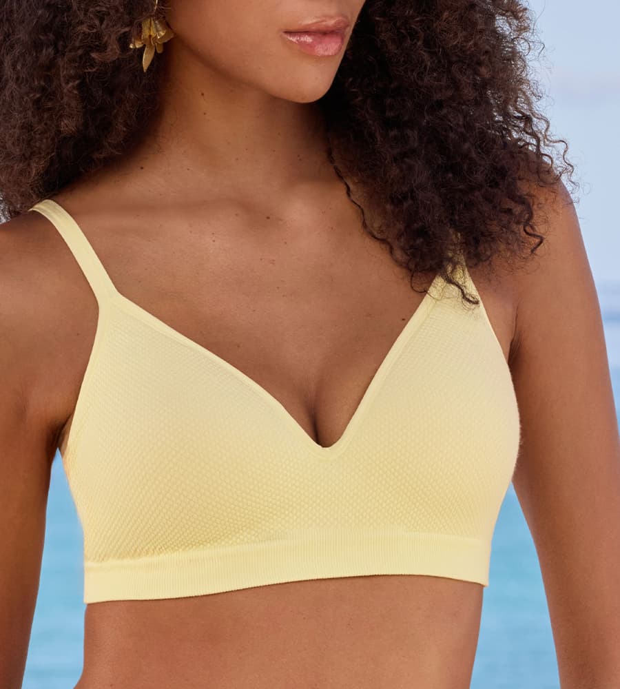 Femme portant un soutien-gorge jaune à fines bretelles, vue de face devant un fond de mer bleue