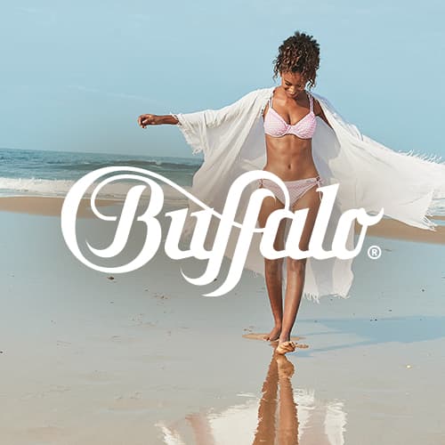 Logo Buffalo – Femme en bikini clair et kimono blanc marchant sur une plage au bord de la mer