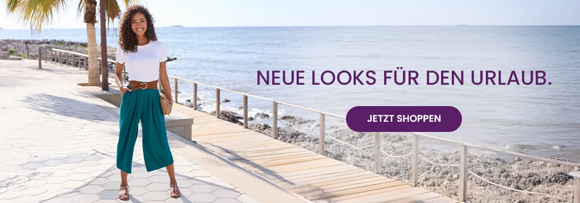 NEUE LOOKS FÜR DEN URLAUB – Frau in weißem Shirt und türkiser Hose steht am Meer auf der Promenade