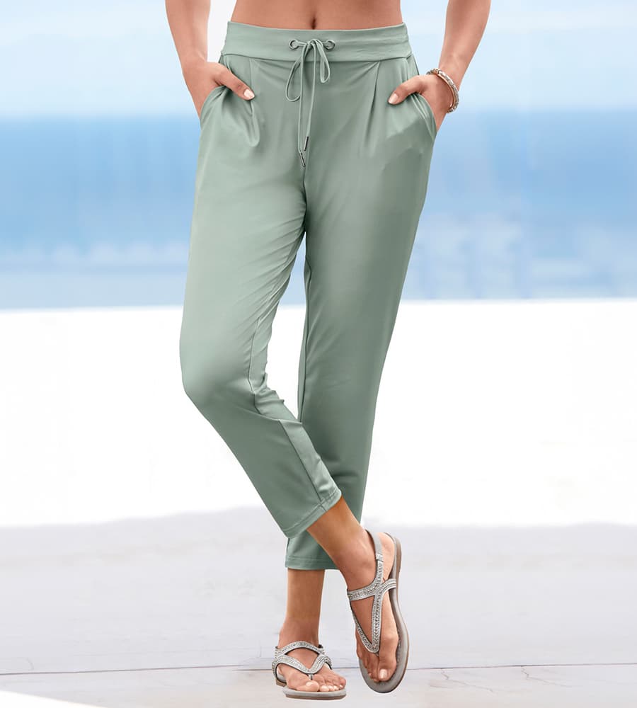 Pantalon vert clair taille haute à cordon, poches latérales, porté avec sandales à brides devant un fond bleu clair