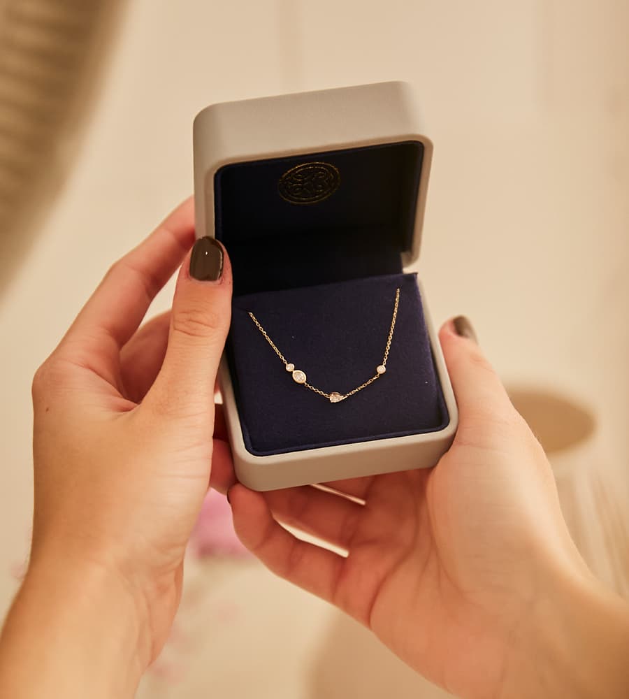 Kette mit drei runden Anhängern in einer grauen Schmuckschatulle, von zwei Händen gehalten